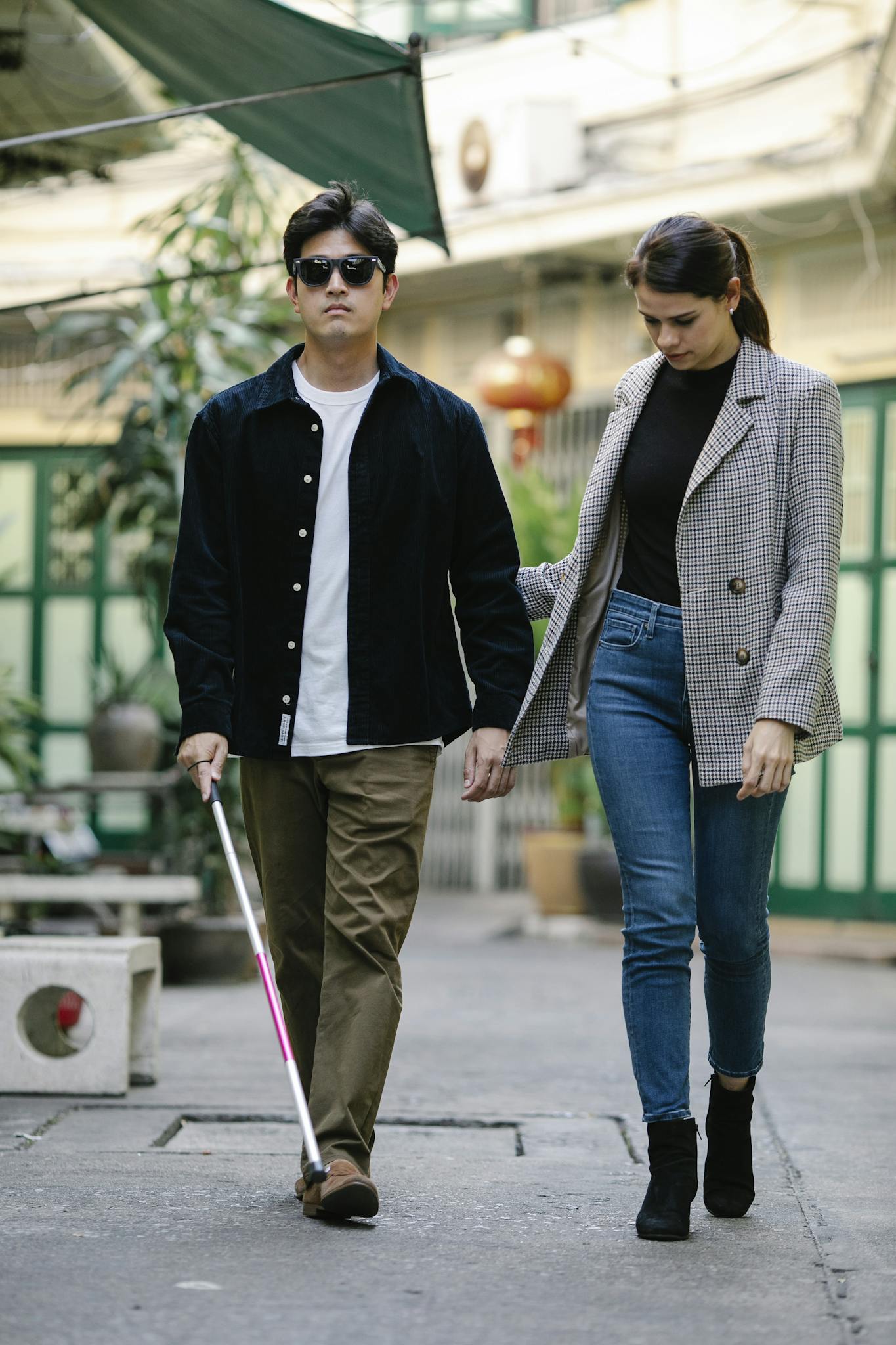 A man with a visual impairment walks with a guiding companion outdoors.