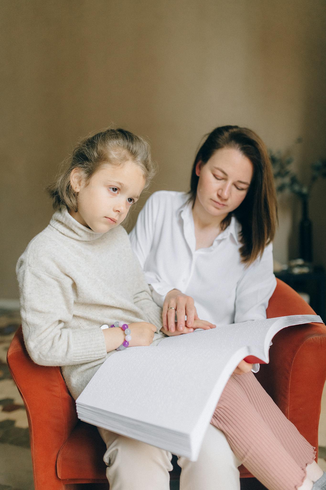 A mother guides her daughter through a braille book, promoting inclusive education.