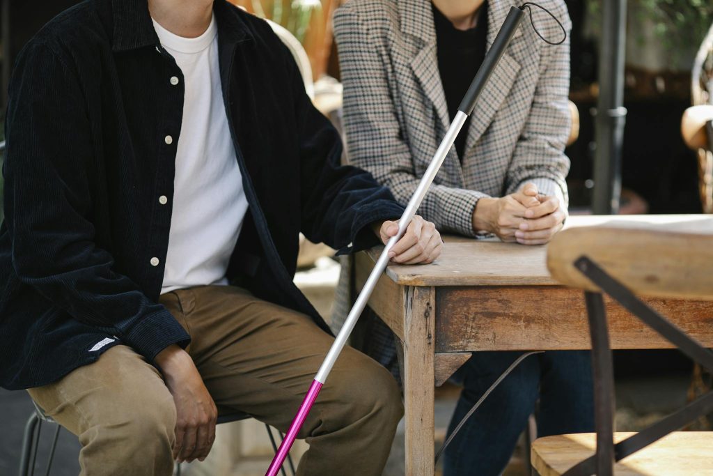 A visually impaired couple sitting together, using a white cane for guidance, at a wooden table indoors.