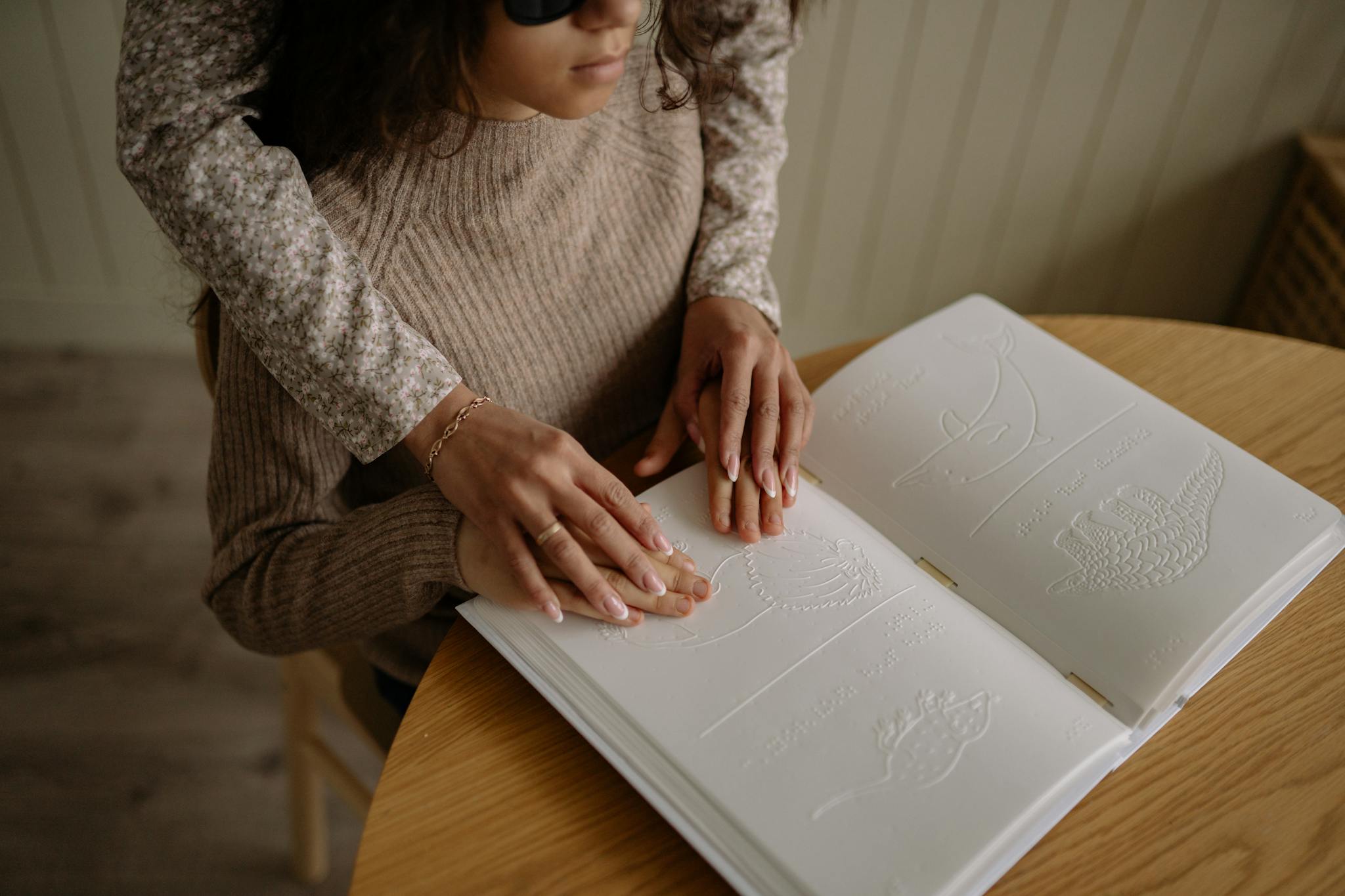 An adult woman learning to read braille with assistance indoors.