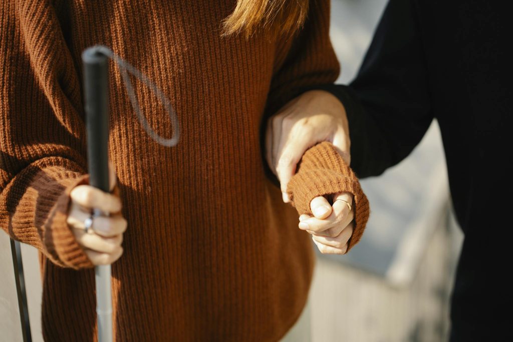 Close-up of two people holding hands, one with a walking cane symbolizing support and visual aid.