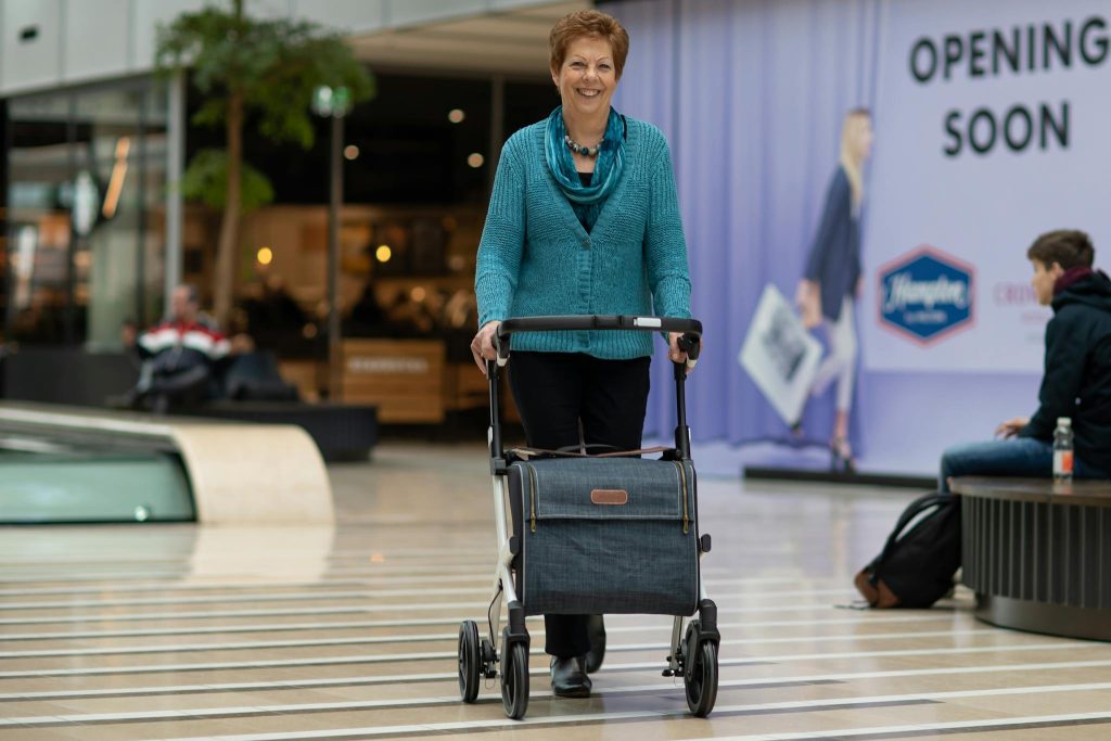 Elderly woman using a rollator walker in a modern shopping mall setting.
